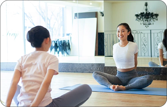 充実した福利厚生を示す写真。2人の女性がスタジオのような場所で笑顔でヨガ（またはピラティス）のポーズをしており、美容、健康、セルフケアに関する福利厚生制度が豊富であることを表現。
